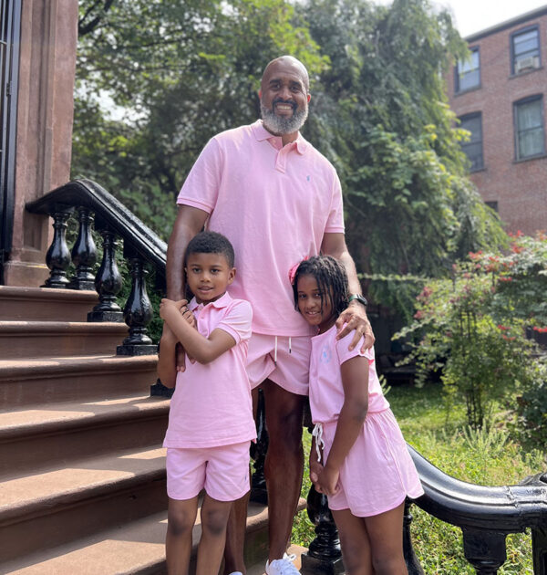 Marlon and two of his three children on a stoop in Central Brooklyn. They are all wearing pink shirts and shorts.